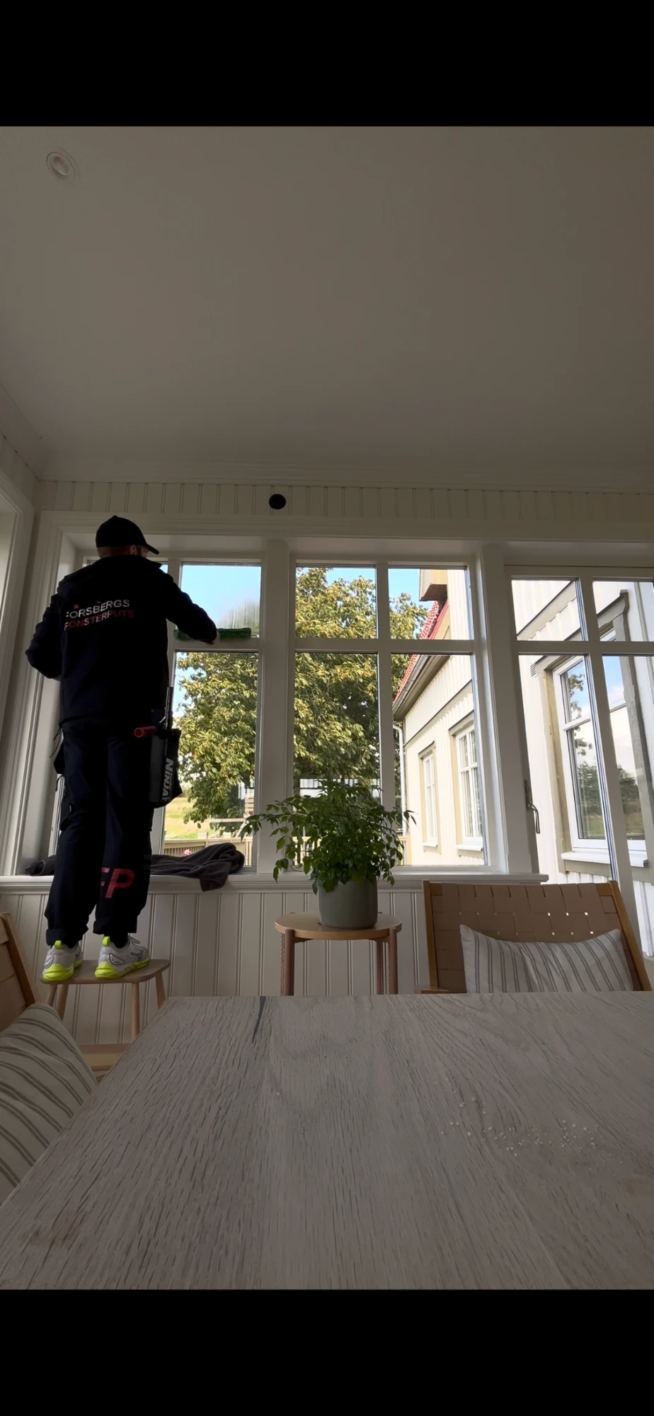 Tommy putsar fönster invändigt i en ljus veranda